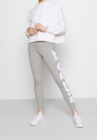 Grå leggings med vit text på sidan, kombinerat med en kortärmad vit hoodie. Outfiten kompletteras av vita sneakers.