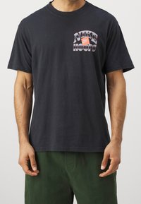 Czarny bawełniany t-shirt z nadrukiem przedstawiającym napis "NIKE HOOPS" w kolorach czerwonym i białym, z okrągłym dekoltem, krótkimi rękawami i luźnym krojem.