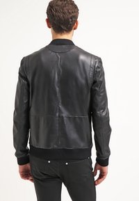 Zwart leren bomberjack, met geribbelde kraag en manchetten, gestructureerd leer op de mouwen, gladde body, getailleerd ontwerp, zichtbare stiksels en accenten.