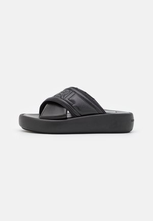 Sort slidesandal med tyk polstret sål og bredt polstret rem med hævede bogstaver.