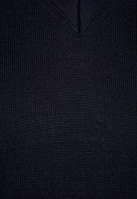 Marineblaues Strickoberteil mit strukturierter Oberfläche, V-Ausschnitt und feiner Rippenstruktur. Das Material wirkt weich und dehnbar.