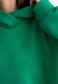 Felpa verde realizzata in tessuto morbido, con un grande cappuccio piegato e polsini a coste; semplice, di un colore uniforme senza motivi o dettagli.