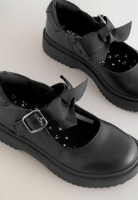 Zwarte Mary Jane-stijl schoenen met een gestructureerd bovenwerk, een dikke rubberen zool en een grote stoffen strik. Binnenvoering met sterpatroon.