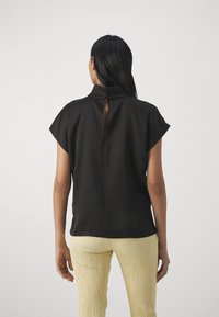 Blusa nera con maniche corte e collo alla coreana, con apertura a chiave sul retro. Texture liscia, design minimalista.