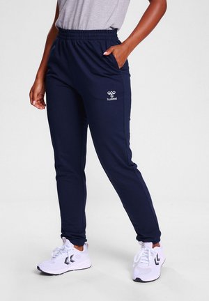Marine joggingsbroek met een elastische tailleband, zijzakken en een wit logo. Gecombineerd met witte sportsneakers en een grijze top.