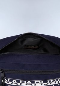 Marineblaue Stoff-Rucksack mit einem Reißverschluss. Das Innere hat ein schwarzes Futter und ein Markenetikett. Auf der Vorderseite ist ein weißer Text zu sehen.