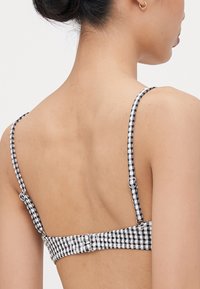 Fekete-fehér kockás mintájú bikini felsőrész állítható pántokkal és hátul zárható csattal. Puha, texturált anyag.
