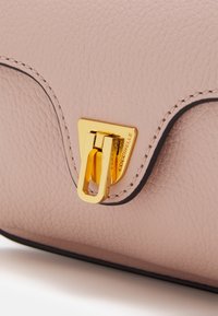 Różowa skórzana torba o fakturze, z złotym metalowym zapięciem, o kształcie trójkąta, z czarnymi wykończeniami i misternym detalem przeszyć.