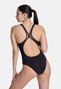 Maillot de bain une pièce noir avec une découpe dans le dos, des bretelles en maille et une texture lisse. Il présente un design simple et une silhouette ajustée.