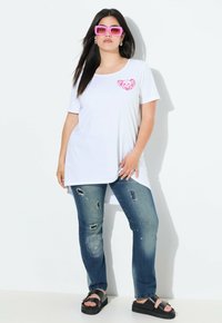 Camiseta blanca de gran tamaño con un gráfico de un oso rosa en el pecho, combinada con jeans azules desgastados y sandalias de plataforma negras. Gafas de sol rosas.
