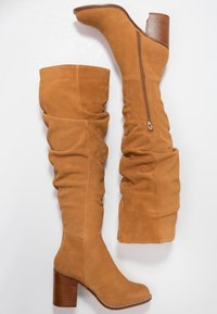 Botas de ante color tostado hasta la rodilla con un diseño arrugado, que cuentan con un zipper lateral y un tacón de bloque de 3,5 pulgadas, mostrando una textura suave.