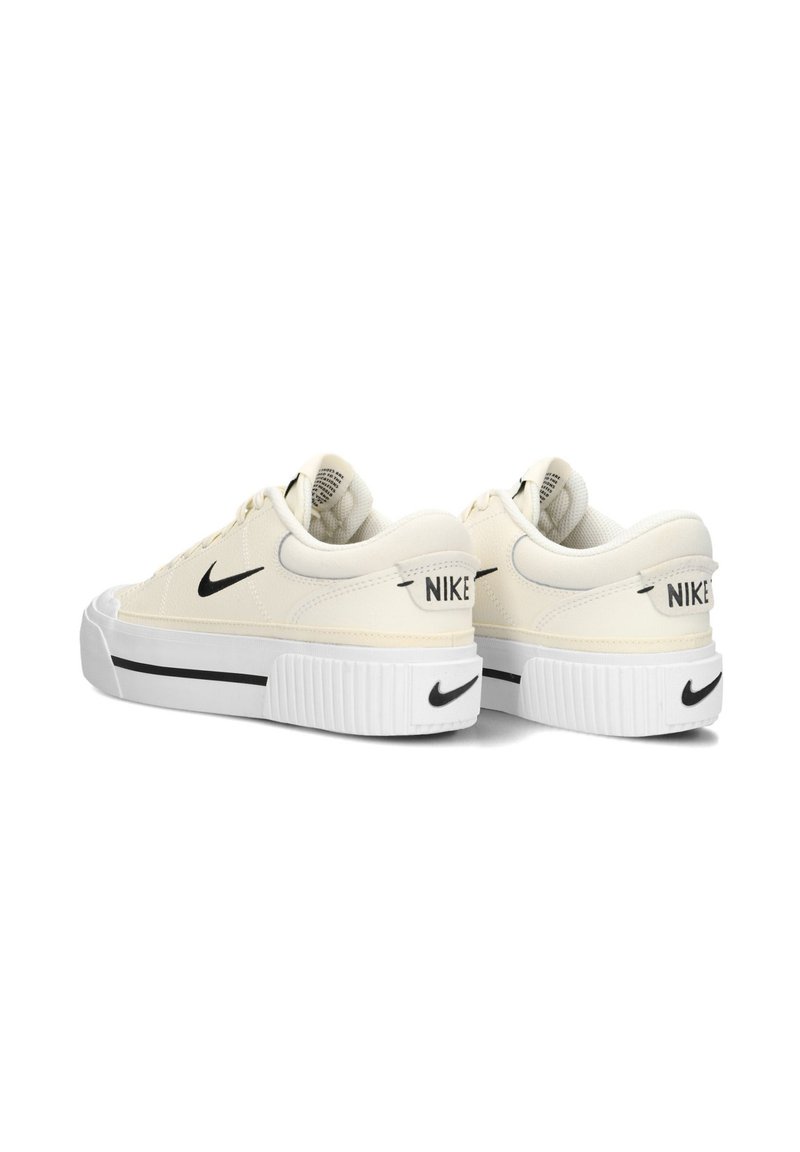 Zapatillas de color crema con una superficie texturizada, que cuentan con un swoosh negro de Nike, suela blanca gruesa y un ligero diseño de plataforma.