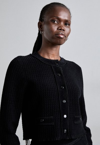 Mustakudottu kardigan, jossa on teksturoitu kudos, pyöreä kaula-aukko, nappikiinnitys, kaksi etutaskua ja aallotettu yksityiskohta.