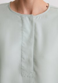 Hellgrüner, weicher Stoffoberteil mit rundem Ausschnitt und einem kurzen Schlitz vorne. Verfügt über saubere Nähte und eine glatte Textur.