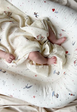 Bébé enveloppé dans une couverture crème avec des motifs sur le thème du cirque, allongé sur un coussin blanc orné de petits motifs d'étoiles et de personnages.