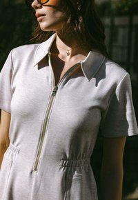 Kortärmad, ljusgrå zip-up klänning med krage, elastisk midja och sidofickor. Tyget har en slät, mjuk textur.