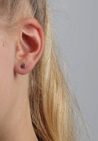 Boucle d'oreille en forme de cœur en violet avec de petites pierres précieuses, montées sur un support en argent, portée sur une oreille partiellement visible.