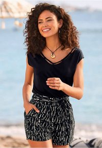 Črna kratka majica s kratkimi rokavi in izrezom ter črno-bele kratke hlače z vzorcem in pasom za zavezovanje. Pripomočki vključujejo zlato ogrlico in uhane.