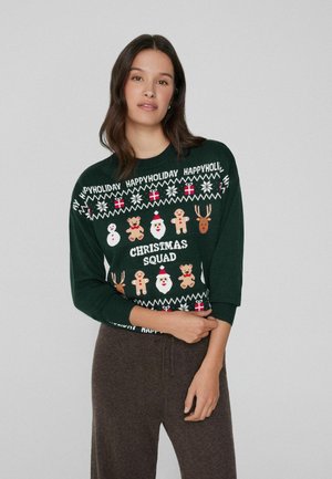 Pull de vacances vert ornée de motifs festifs tels que des bonhommes de neige, le Père Noël, des rennes et des house de pain d'épices. Tissu doux avec des manches trois-quarts.