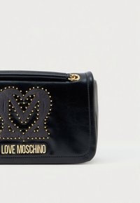 Juodos dirbtinės odos rankinė su auksinio atspalvio logotipu ir pūstytu širdies raštu. Stačiakampio formos, su užtrauktuku ir šoninėmis siūlių detalėmis.