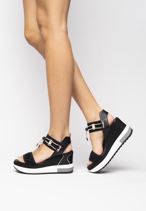 Zwarte sleehakken met open teen, voorzien van een textuur bovenwerk, verstelbare enkelbandjes en witte zolen met een grijze accenten.