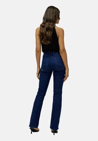 Jean taille haute bleu foncé avec une jambe évasée, tissu texturé et coutures marquées sur les poches arrière. Assorti à un haut noir.
