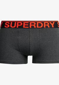 Męskie bokserki w ciemnoszarym materiale o gładkiej fakturze. Czarny pas z logo "SUPERDRY" w wyraźnym czerwonym napisie.