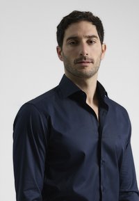 Camisa azul marino de corte slim, de manga larga y cuello clásico. Presenta una textura suave y un logo discreto en el pecho.