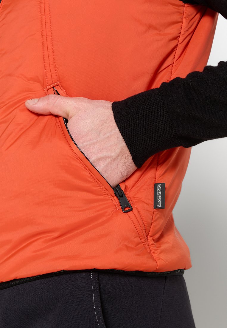 Pomarańczowa kamizelka puchowa z zamykaną kieszenią i czarnymi dzianinowymi mankietami. Wykonana z gładkiego, wodoodpornego materiału i lekkiej izolacji.
