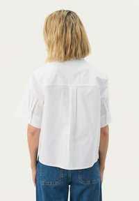 Korte mouwen witte blouse met een ontspannen pasvorm, voorzien van een rugpand, een zachte textuur en knoopaccenten op de opgerolde mouwen.