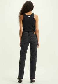 Top negro sin mangas y vaqueros negros de tiro alto con corte recto. El denim presenta un parche de cuero y un ligero deshilachado en los bordes.