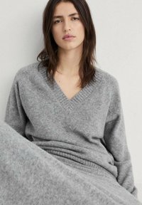 Grauer, gestrickter Pullover mit V-Ausschnitt und Rippdetails, ausgestattet mit einer weichen Textur und lockerer Passform, ergänzt durch einen passenden grauen Rock.