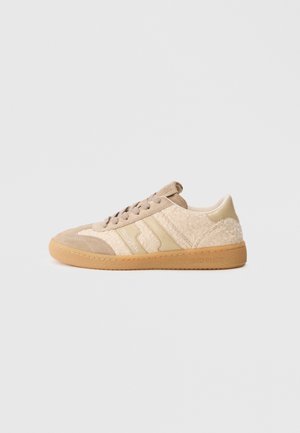 Beige sneakers featuring a mix of suede and textured fabric, with a gum sole and contrasting beige stripes. Round toe and lace-up design.