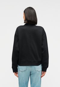 Μαύρο φαρδύ φουτερ με ψηλό γιακά, ριμπ μανσέτες και τελείωμα. Λείο υφή, σχεδιασμένο με άνετη γραμμή. Συνδυασμένο με ανοιχτόχρωμο μπλε τζιν.