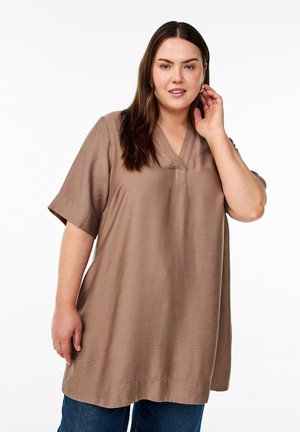 Brown tunic top with short sleeves, v-neckline, and a relaxed fit, made of a smooth material with a subtle texture. Paired with blue jeans.