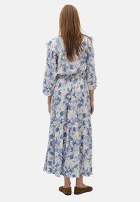 Kukallinen maxi-mekko vaaleansinisissä sävyissä, jossa on röyhelökaulus, elastinen vyötärö ja kolmen neljänneksen hihat. Pehmeä, virtaava kangas.