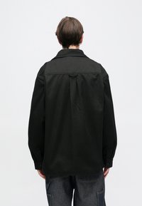 Czarna bawełniana koszula o luźnym kroju, z ostro zakończonym kołnierzykiem i mankietami zapinanymi na guziki. Gładka faktura i prosty design bez zdobień.
