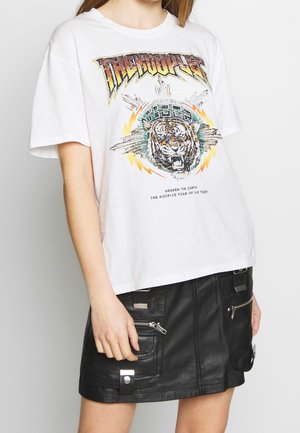 Weißes übergroßes T-Shirt mit buntem, brüllendem Tiger-Print und Text, kombiniert mit einem schwarzen Leder-Minirock mit Reißverschluss- und Schnallendetails.