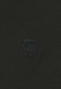 Must mustriba kangas, millel on peene tume logo, sujuva tekstuuri ja tihe sobivus. Kujundus on minimalistlik, ilma lisamusterideta.