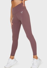 Leggings a vita alta in un mauve tenui, realizzati in un tessuto morbido ed elastico. Presentano un logo discreto e dettagli di cucitura verticale lungo le gambe.