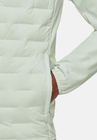 Jasnozielona kurtka puchowa z fakturowanym pikowanym wzorem, elastycznymi mankietami i boczną kieszenią na zamek. Gładki materiał o nowoczesnym kroju.