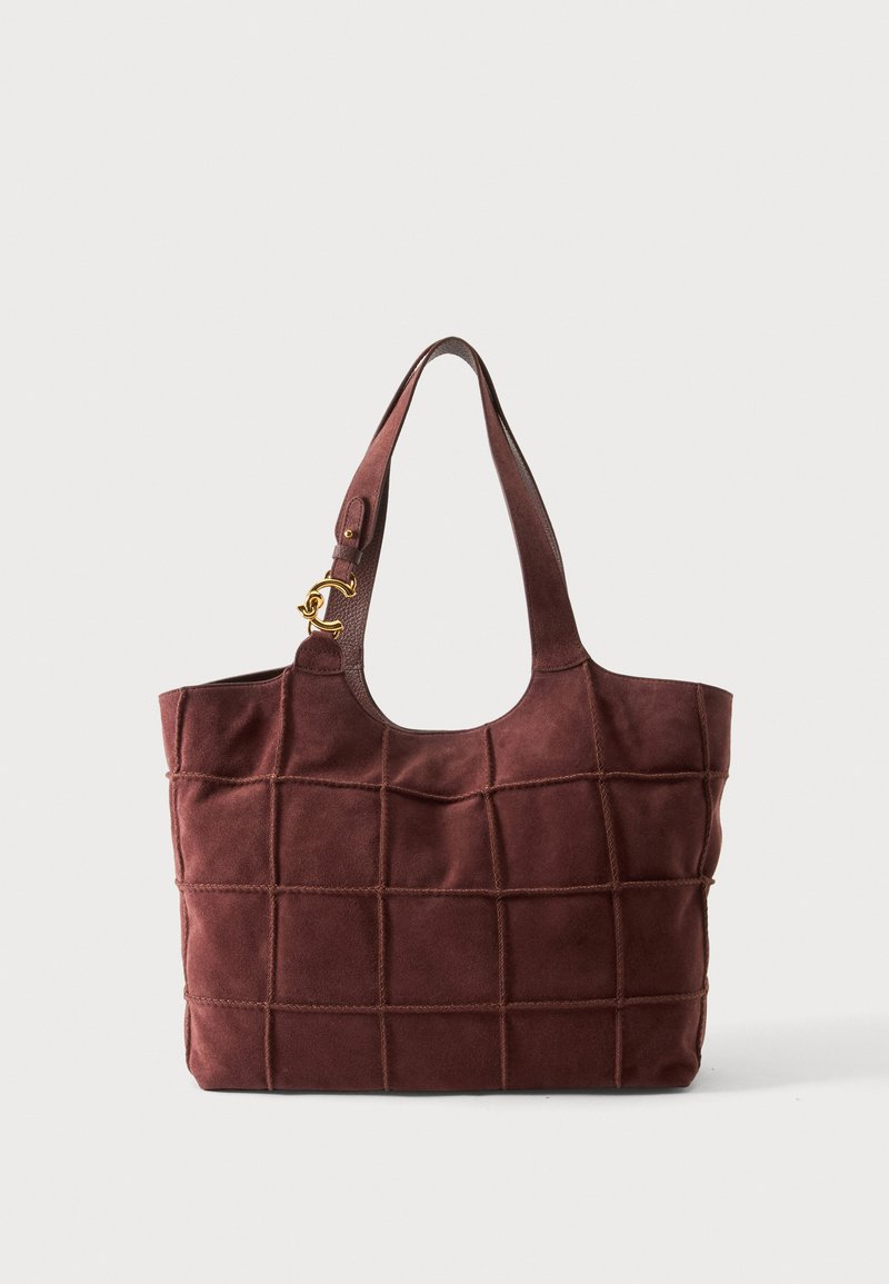 Sac cabas en daim marron avec surpiqûres en quadrillage, anses larges et petit charm logo doré sur une bandoulière.