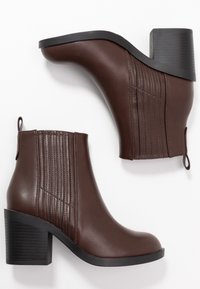 Brązowe skórzane botki do kostki z okrągłym noskiem, teksturowanym panelem oraz masywnym czarnym obcasem. Posiadają pętle do łatwego zakładania.