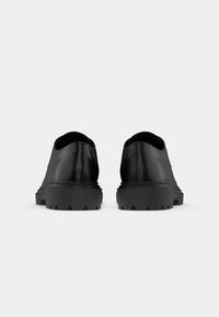 Pantofi din piele neagră cu un finisaj neted, talpă exterioară groasă din cauciuc negru și design minimalist; vârf rotund, detalii de cusătură vizibile pe toc.