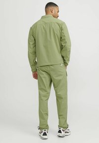 Ljusgrön lättviktsjacka och byxor i andningsbart tyg; har en enkel design med ett elastiskt midjeband och fickor.