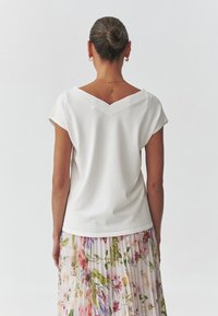 Maglietta bianca a scollo a V con maniche corte, abbinata a una gonna a pieghe floreale con vari colori e motivi. Tessuto morbido e leggero.
