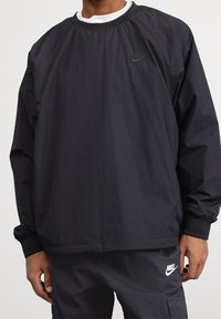 Black Nike pullover sweatshirt with a crew neck, long sleeves, elastic cuffs, and a subtle logo on the chest. Smooth, lightweight fabric.