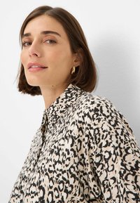 Camicia a maniche lunghe con stampa leopardata, caratterizzata da uno sfondo crema con motivi neri, realizzata in tessuto leggero, con colletto e vestibilità morbida.