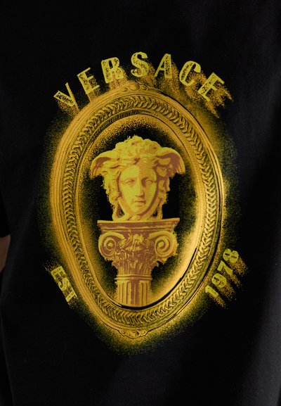 Yellow Medusa head and ornate column design with "VERSACE" above and "EST 1978" below on black fabric background.