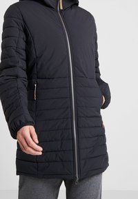 Černá vyp padded bunda s kapucí, která má prošívanou strukturu, stříbrný zip a dvě boční kapsy se zipovými detaily.